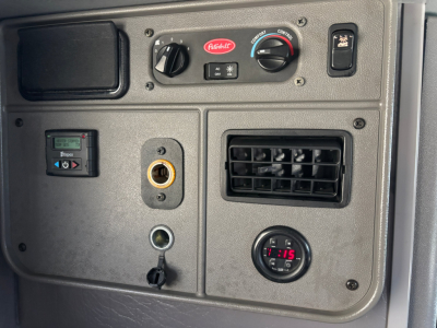 Peterbilt 389 dashboard panel showing climate controls, gauge, 12V outlet, air vent, and various switches in a sleeper truck interior.