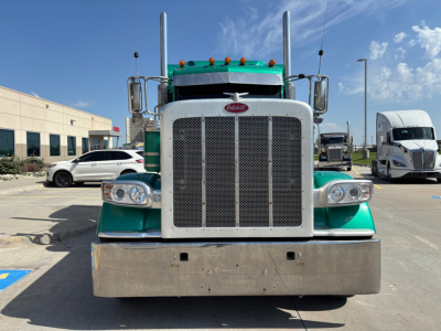 Peterbilt 389 front view showing large chrome grille, Peterbilt emblem, dual tall exhaust stacks, green cab, wide metal bumper.