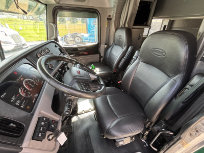 Peterbilt 389 truck interior showing steering wheel, dashboard, and two black leather seats with grey trim.