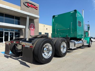Peterbilt 389 tractor in green with sleeper cab, dual rear axles, chrome fuel tanks, viewed from rear side showing wheels and mud flaps.