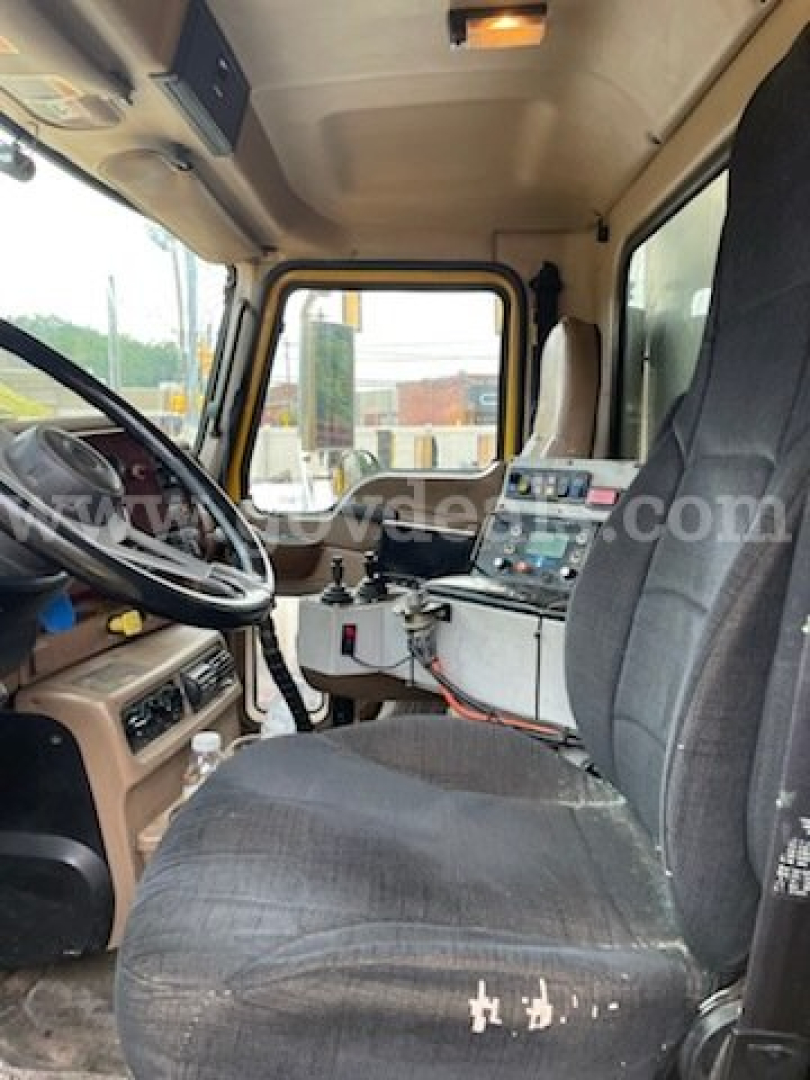 Cab interior of a 2006 Mack CV713 dump truck showing steering wheel, dashboard, and driver seat with controls and wiring panel.