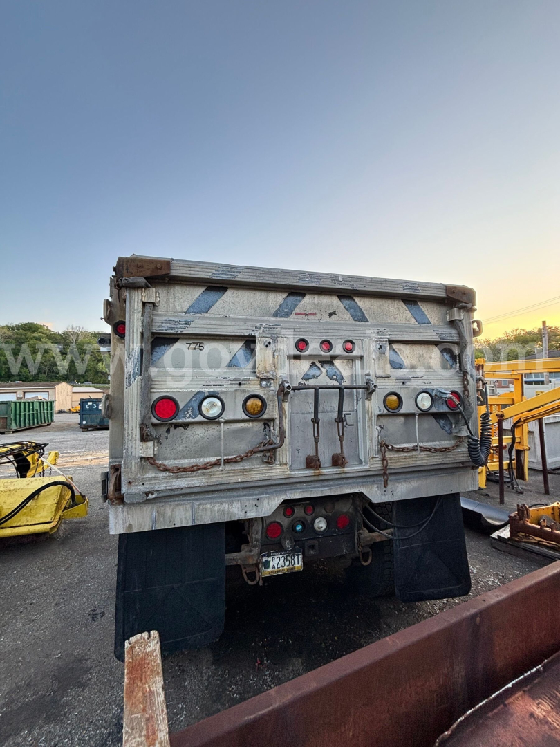 Dump truck rear showing tailgate with multiple taillights, reflective chevrons, and towing equipment mounted on a weathered aluminum body.