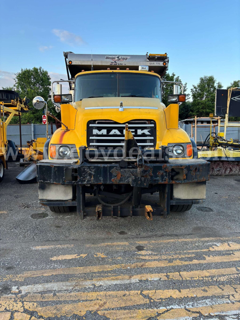 Front view of a yellow Mack CV713 dump truck showing grille, headlights, bumper, and mounted plow; visibility of cab and hood with Mack logo.