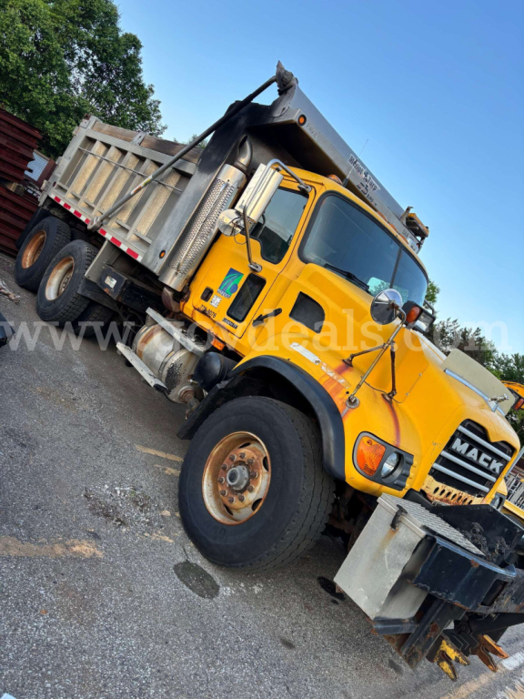 Mack CV713 dump truck side/front view showing bright yellow cab and silver dumping bed with black grille and large tires.
