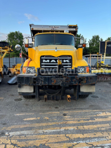 Front view of a yellow Mack CV713 dump truck showing grille, headlights, bumper, and mounted plow; visibility of cab and hood with Mack logo.