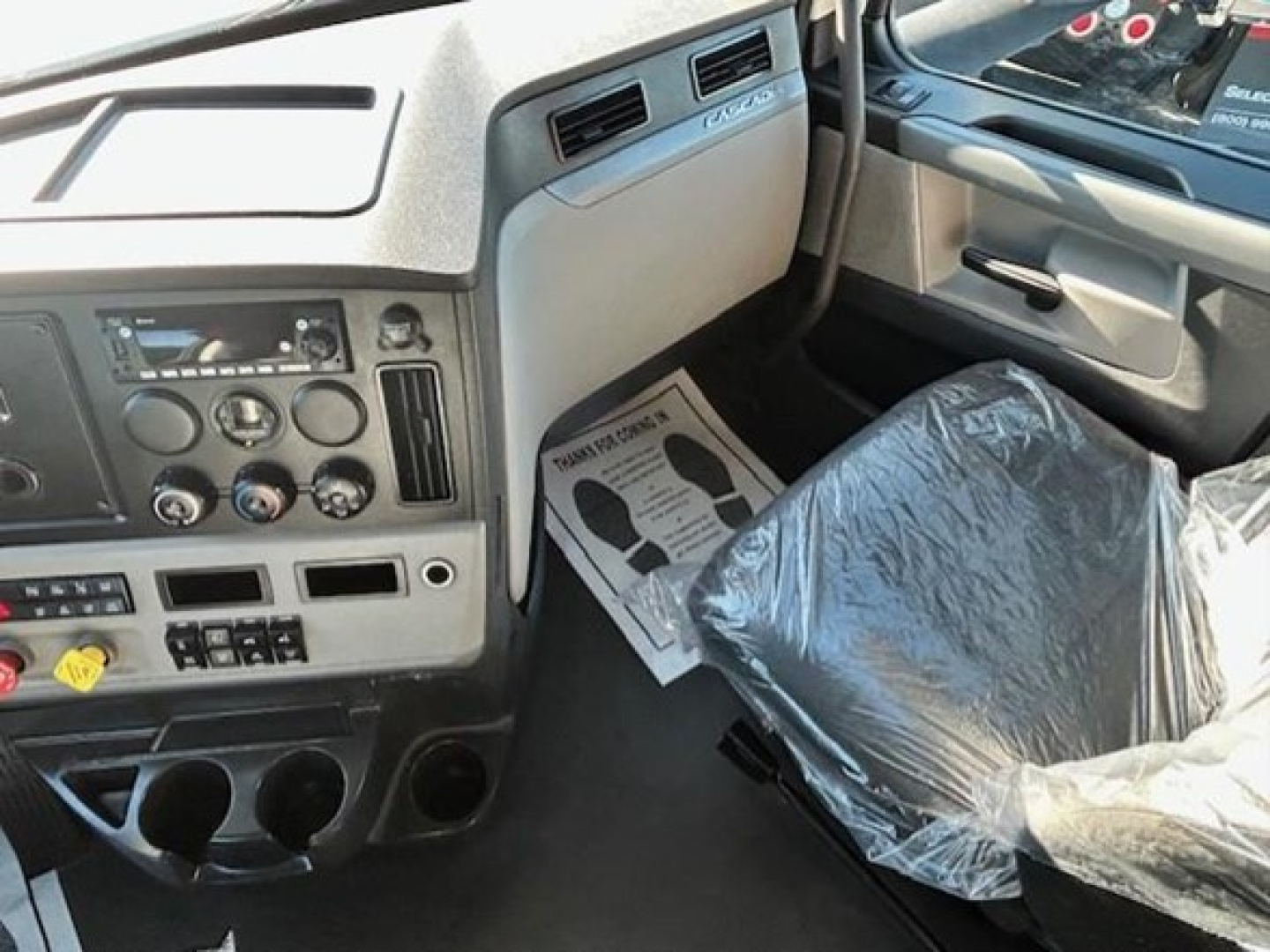 Freightliner Cascadia 116 truck interior dash area and driver's seat with plastic cover and center console visible.