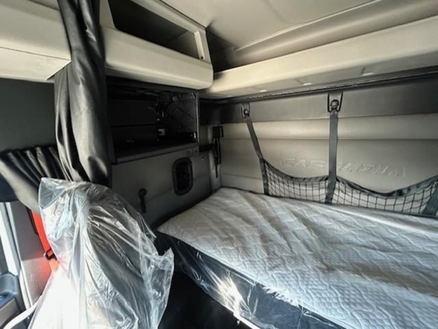 Freightliner Cascadia 116 sleeper cab interior showing bunk bed with mattress and overhead storage shelf.