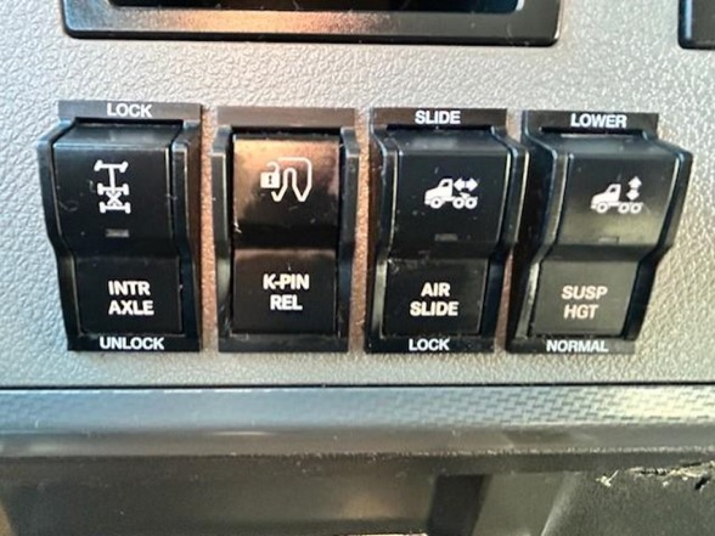 Dashboard switches showing lock, intraxle, K-pin rel , air slide, lower, and suspension heat functions in Freightliner Cascadia cabin.