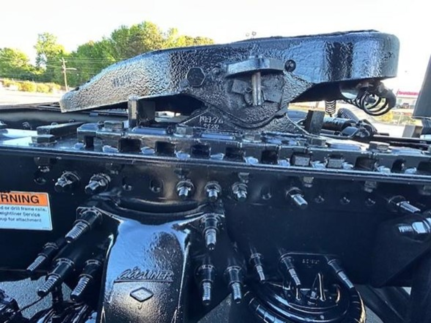 Tractor-trailer engine bay area with hydraulic lines and a prominent hitch assembly. Visible text on components includes 'CATLINE' or similar branding on a cylindrical part and various bolts and hoses.