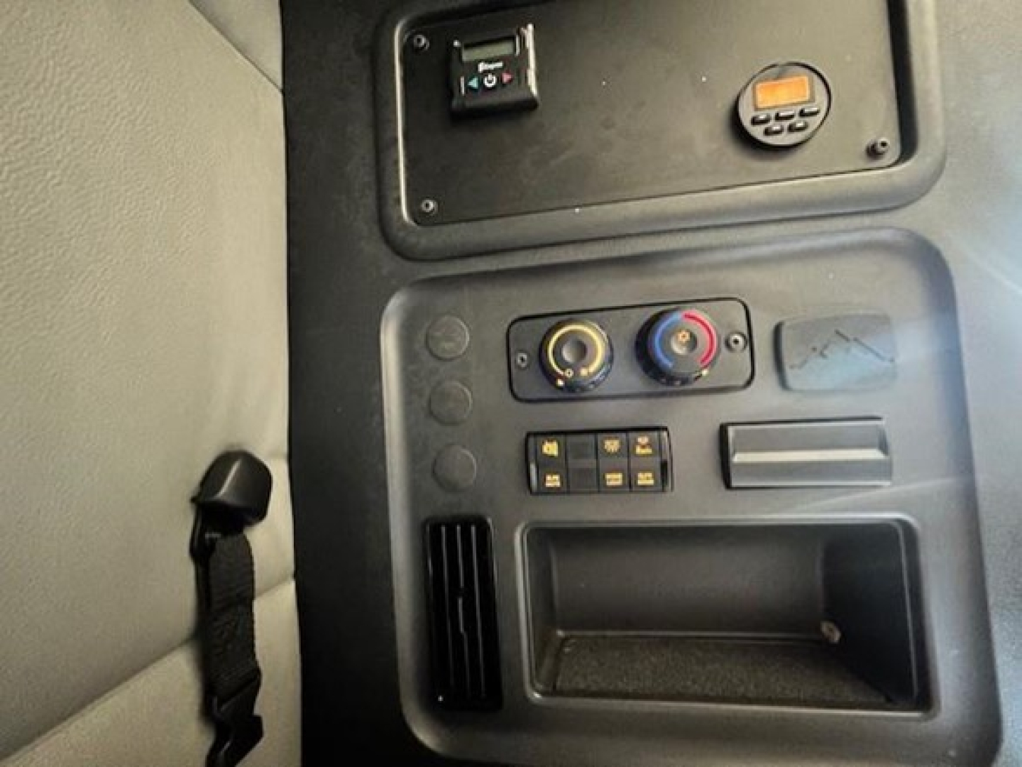 Cab interior of a Freightliner Cascadia showing control switches, circular climate knobs, storage pocket, and vent; part of dash area visible.