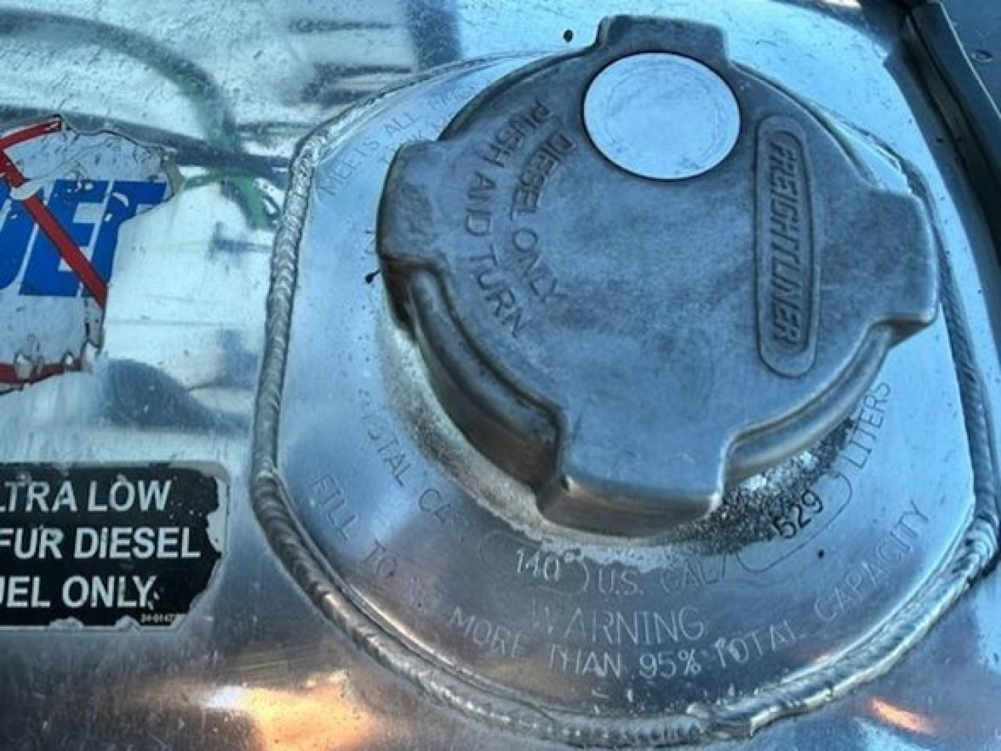 Fuel/water filler cap on Freightliner Cascadia engine bay with surrounding labels and warning text.