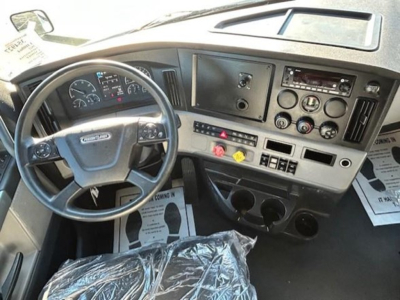 Cab interior of a Freightliner Cascadia 116 showing steering wheel, dashboard with gauges, controls, and cup holders.