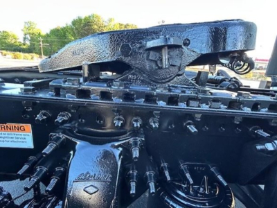 Tractor-trailer engine bay area with hydraulic lines and a prominent hitch assembly. Visible text on components includes 'CATLINE' or similar branding on a cylindrical part and various bolts and hoses.