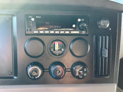 Dashboard panel of a Freightliner Cascadia showing radio readout 94.9 MHz, three circular gauges, and climate controls.