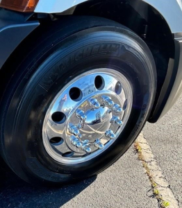 Front wheel and chrome hubcap of a Freightliner Cascadia 116, with black tire and polished chrome wheel.