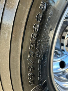 Wheel and tire sidewall with size 225/75R25 slanted text and small markings visible on the tire bead.