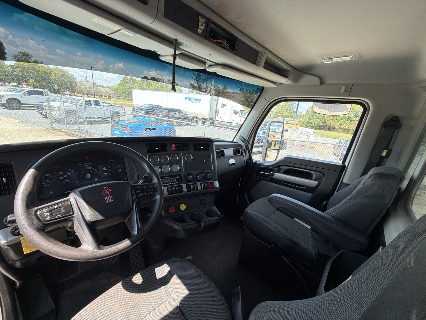 Kenworth T880 truck cockpit interior with steering wheel, dashboard, and driver seat; view through windshield and side window showing exterior lot.