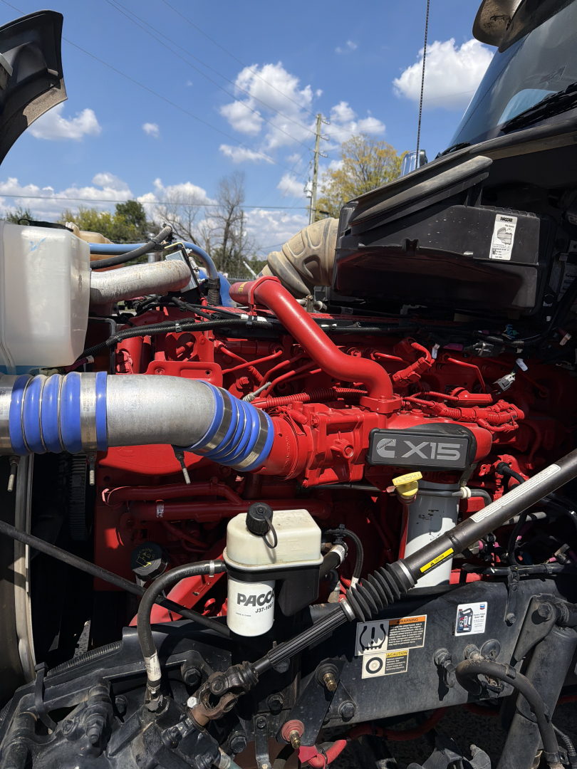 Kenworth T880 engine bay showing red Cummins X15 engine with blue hoses and black components.