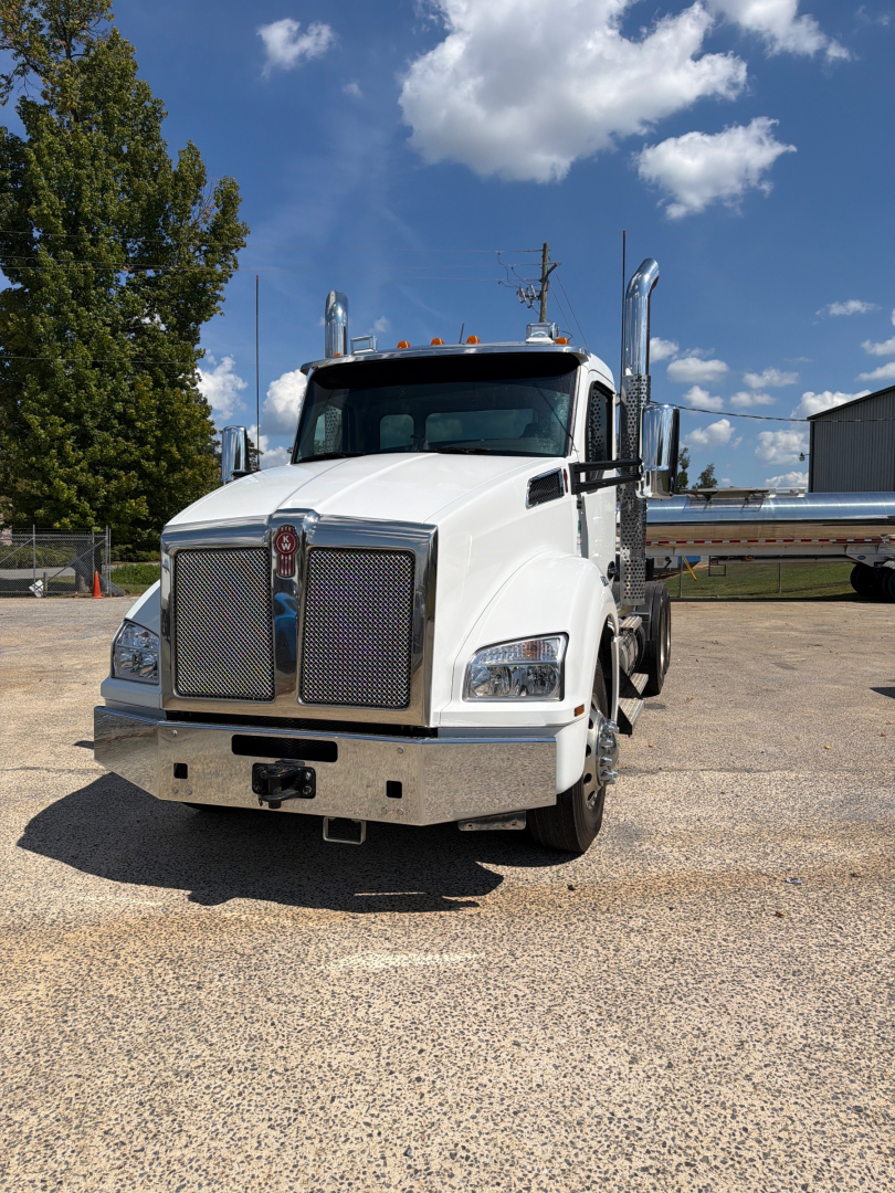 Kenworth T880 conventional daycab truck front view, white paint, chrome grille, headlights, large bumper, dual exhaust stacks, VIN tag not visible.