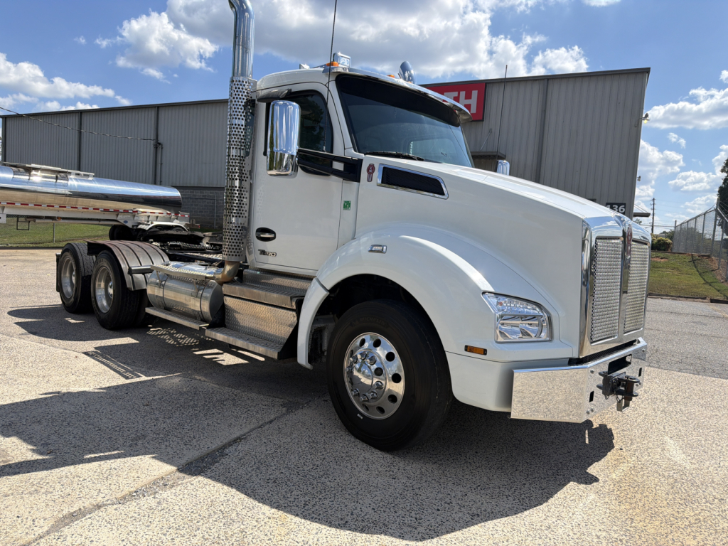Kenworth T880 conventional daycab truck in white, side view with chrome exhaust stacks and fuel tanks, front grille, windshield, and wheels visible.