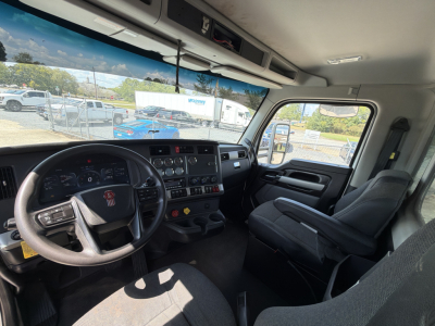 Kenworth T880 truck cockpit interior with steering wheel, dashboard, and driver seat; view through windshield and side window showing exterior lot.