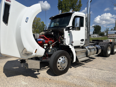 Kenworth T880 conventional daycab truck with hood open showing engine bay and front left wheel; visible components include red engine parts and chrome exhaust stack.