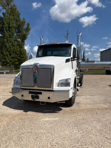 Kenworth T880 conventional daycab truck front view, white paint, chrome grille, headlights, large bumper, dual exhaust stacks, VIN tag not visible.