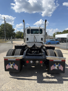 Kenworth T880 rear view showing fifth-wheel area and dual rear axles; flags on mud flaps; grey cab; clear sky
