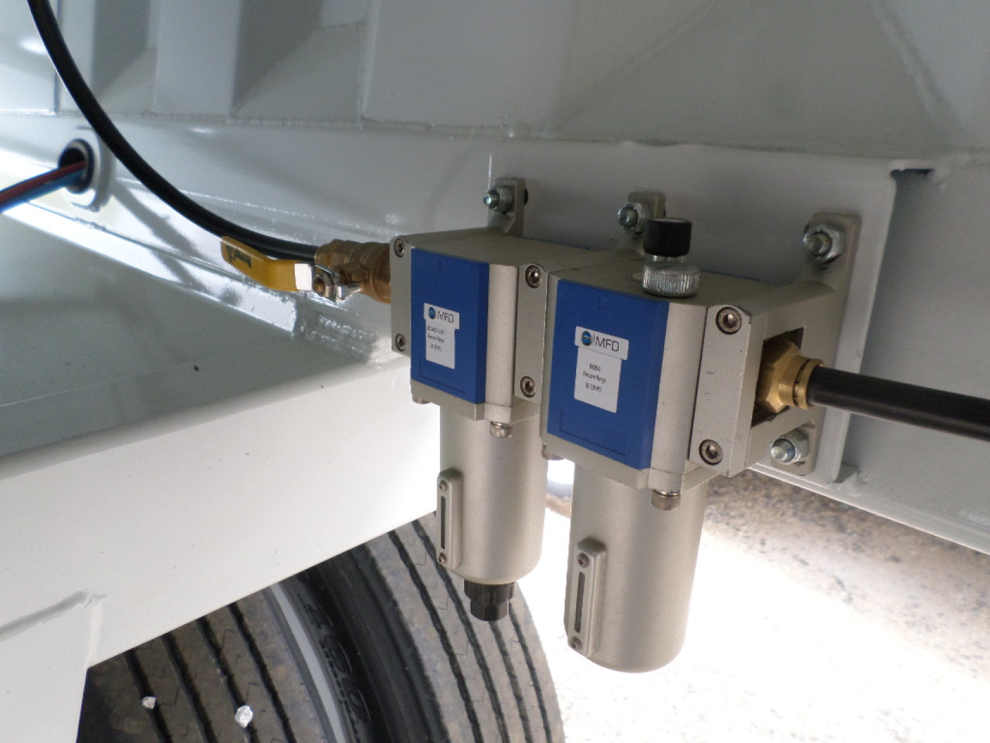 Dual air line quick-release valves mounted under a dump trailer, with blue-and-silver valve bodies and cylindrical filter-like components, hoses connected.