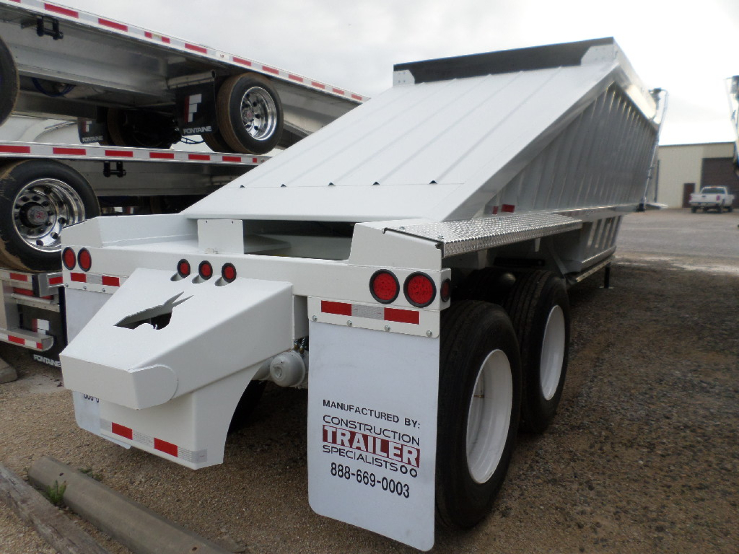 Trailer dump bed showing white body with dual rear axles and hydraulic mechanism label from Construction Trailer Specialists.
