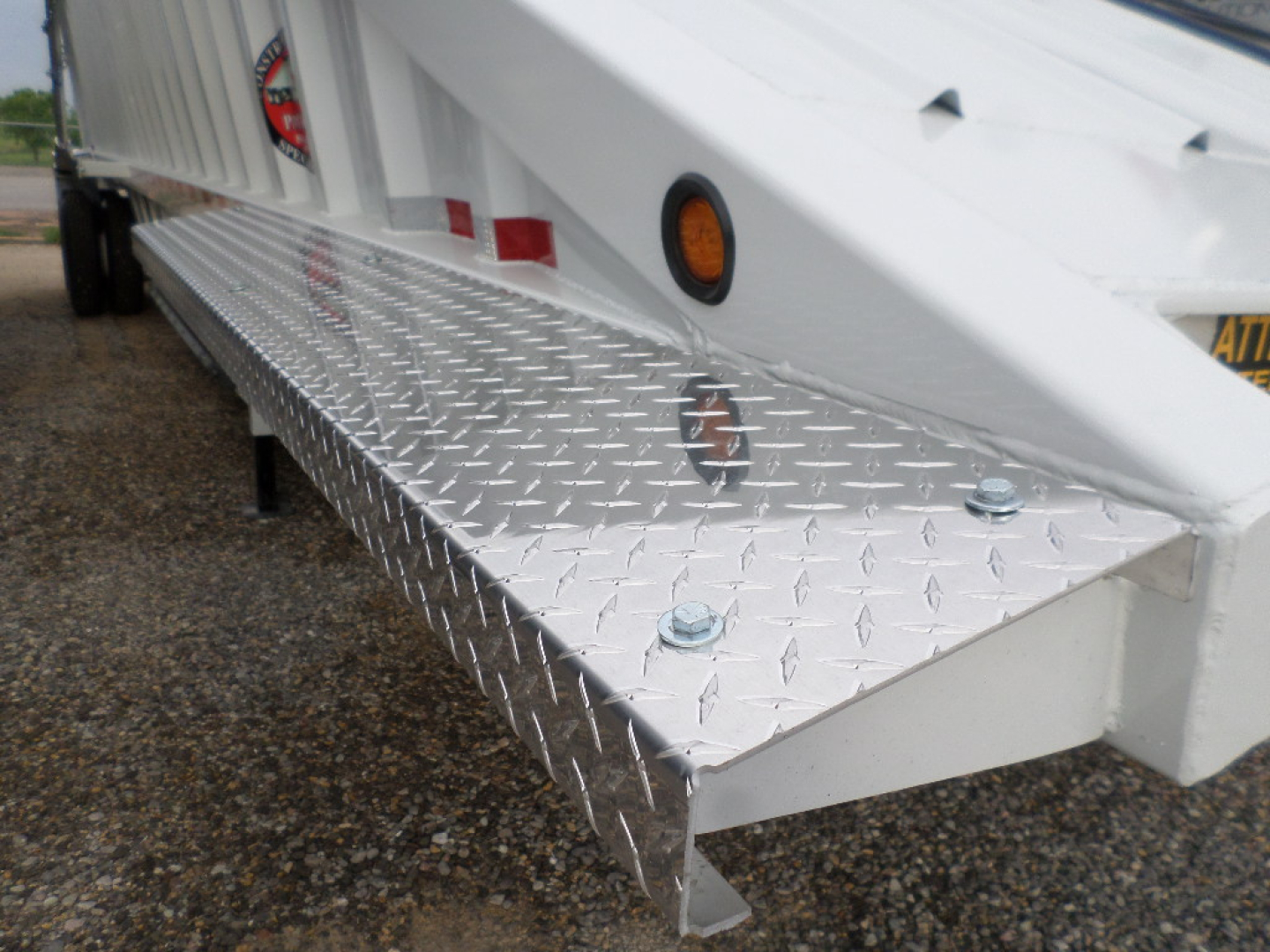 Trailer side view showing diamond plate step with bolts and white trailer body.