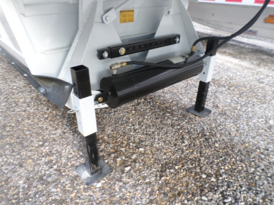 Trailer undercarriage showing hydraulic air-ride suspension cylinder and support legs with black hydraulic tank and fittings.