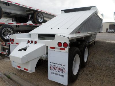 Trailer dump bed showing white body with dual rear axles and hydraulic mechanism label from Construction Trailer Specialists.