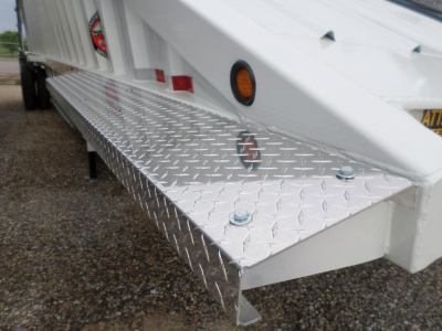 Trailer side view showing diamond plate step with bolts and white trailer body.