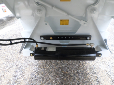 Trailer rear with air ride suspension and hydraulic component; black cylindrical actuator; warning labels on white frame; hoses connected.
