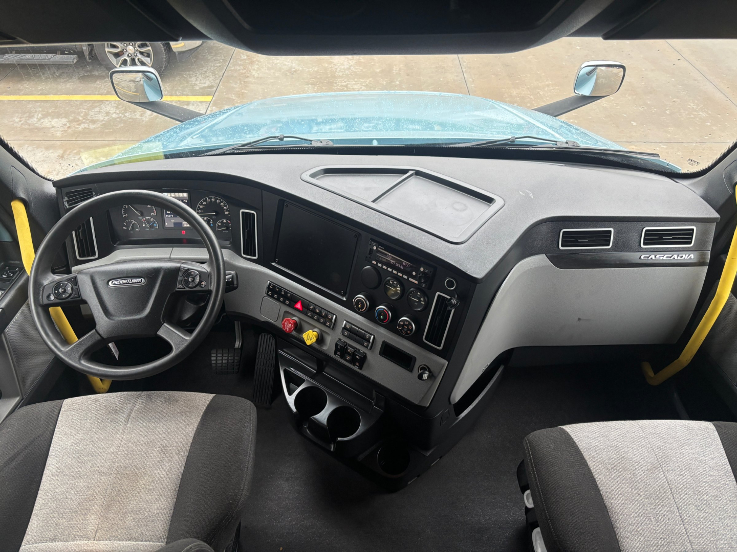 Truck cab interior of a Freightliner; steering wheel, dashboard, center console, and driver and passenger seats visible.