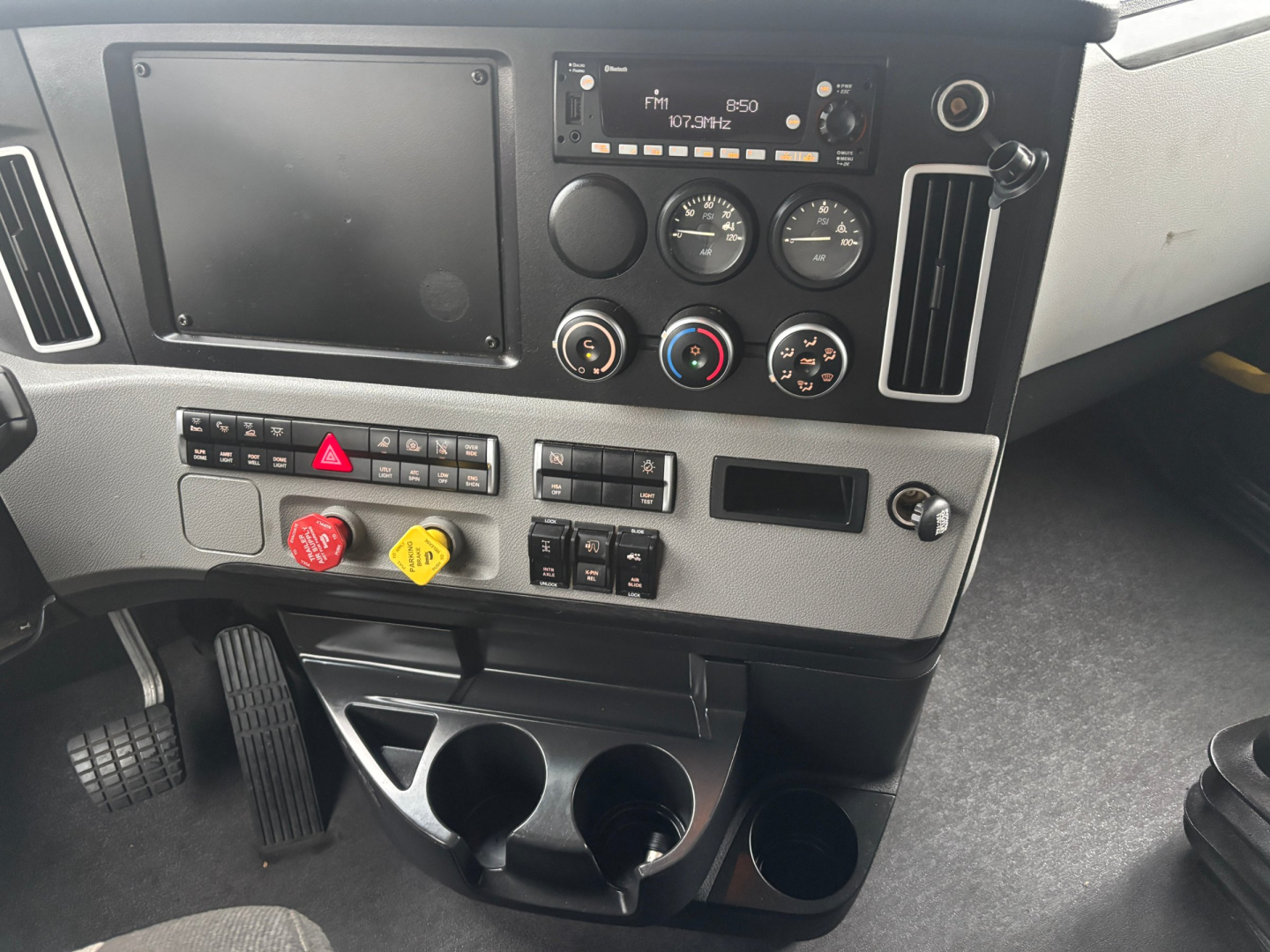 Dashboard of Freightliner PT126064ST showing radio, gauges, climate controls, switches, and cup holders.