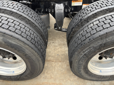 Dual rear axles of a Freightliner truck showing two large tires and the suspension components between them, part of the chassis visible.