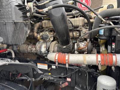 Conventional sleeper truck engine bay showing multiple hoses, belts, and a red-painted intercooler hose with clamps.