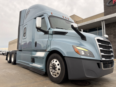 Freightliner semi tractor in light blue showing front left side with aerodynamic mirrors and large black bumper; cab with sleeper, wheel, and wheel covers visible.