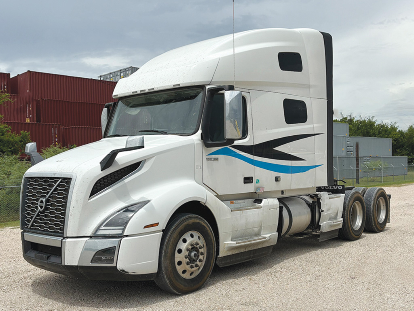 Volvo VNL 860 truck in white with blue and black graphics, side view showing cab and sleeper, chrome grille, fuel tanks, and dual rear axles.