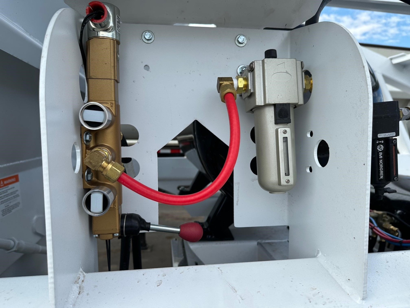 Trailer hydraulic system and valve block with lines and fittings in a white dump trailer bay showing brass manifold and electric valve