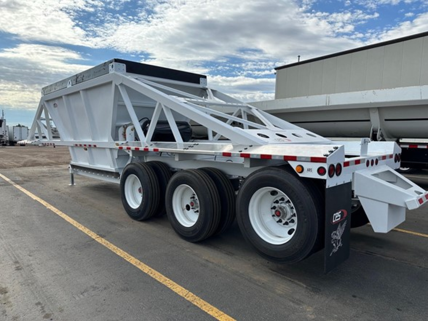 Tri-axle bottom dump trailer with white frame and multiple support beams, rear mudflaps, and triple axle configuration.