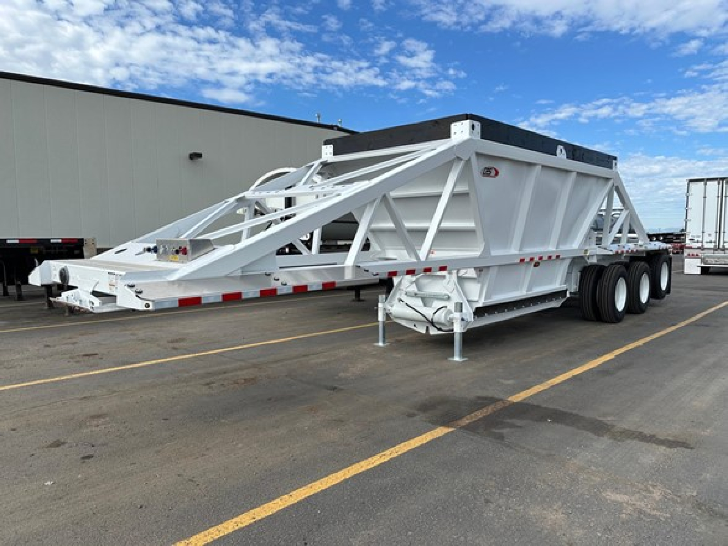 Bottom dump trailer in a parking lot showing white steel frame and tri-axle configuration with rear hydraulic dump bed and front hitch.