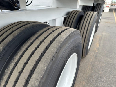 Bottom-dumper trailer dual-axle tires visible, side view of tri-axle chassis with multiple wheels, part of air-ride suspension system.