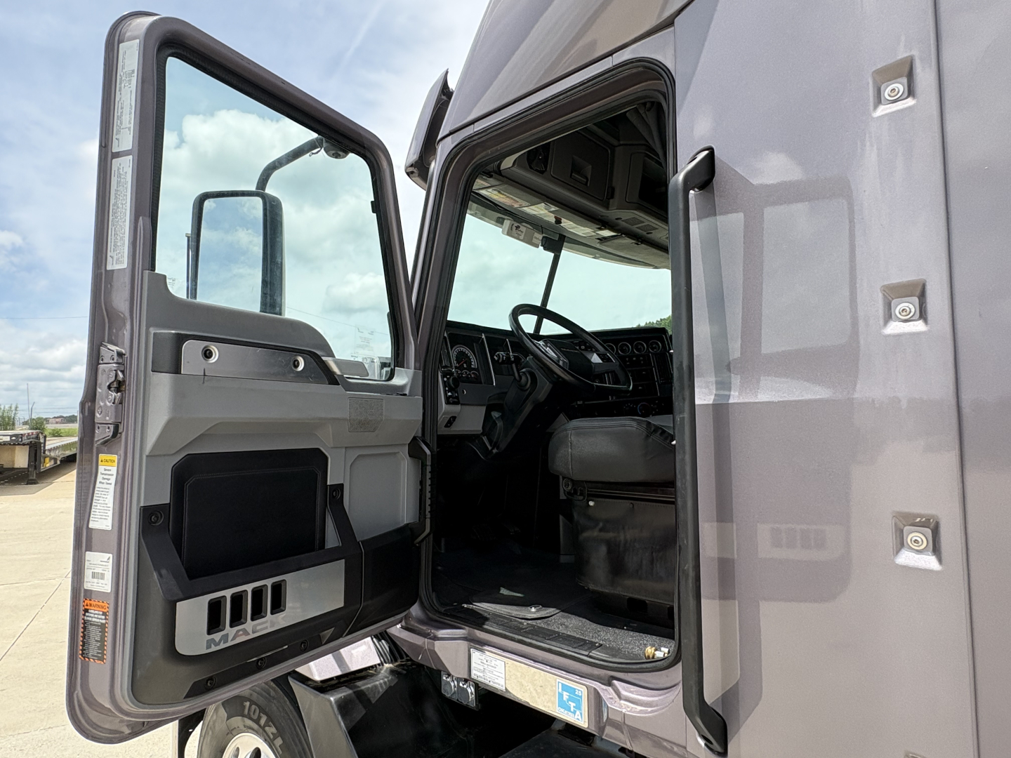 Mack AN64T70 truck cab interior view through open driver door showing steering wheel and dashboard.