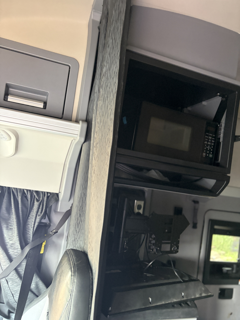 Mack AN64T70 sleeper truck cab interior showing overhead cabinet with microwave, small display, and storage compartments.