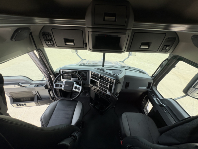 Truck cab interior of a 2024 Mack AN64T70 from the driver’s seat view, with steering wheel, dashboard, gauges, and overhead console visible.