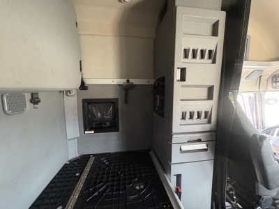 Conventional sleeper truck cab interior showing storage cabinets and dashboard area with electrical panel and windows