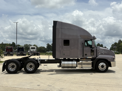 Truck chassis side view showing a gray Mack AN64T70 sleeper with cab, mid-frame fuel tanks, and dual rear axles.